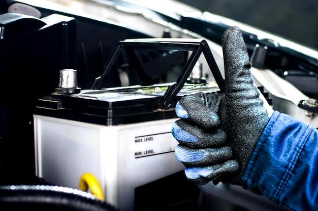 Il meccanico alza con sicurezza il pollice accanto alla batteria